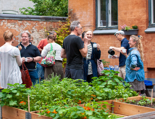 Gruppe af mennesker taler sammen og drikker kaffe foran et gult hus, Apostelkirken