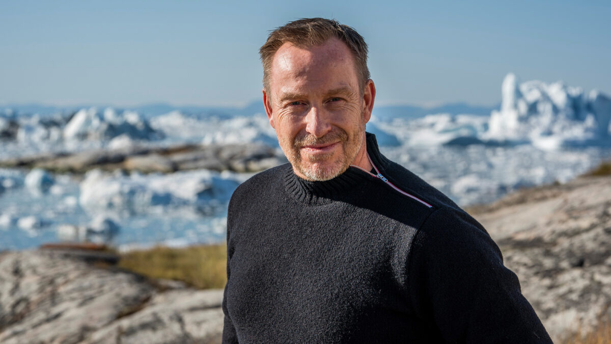 Portræt af Adam Price. Man i blå sweater kigger ind i kameraet. Hav og is i baggrunden.